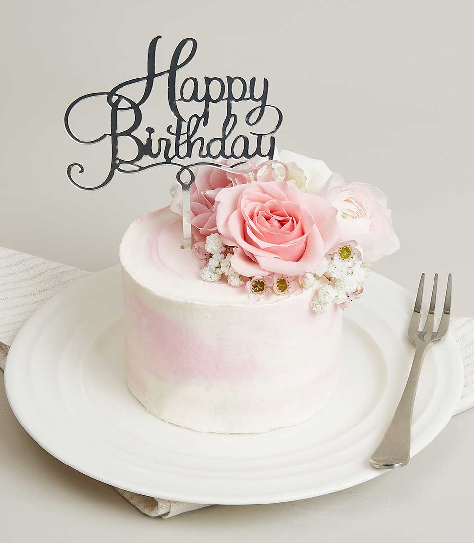 Mini pink rose birthday cake with fresh flowers and white marble frosting on ceramic plate