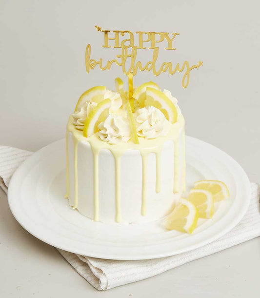 Lemon white cream mini cake with frosting swirls, lemon slice garnish, and gold birthday topper