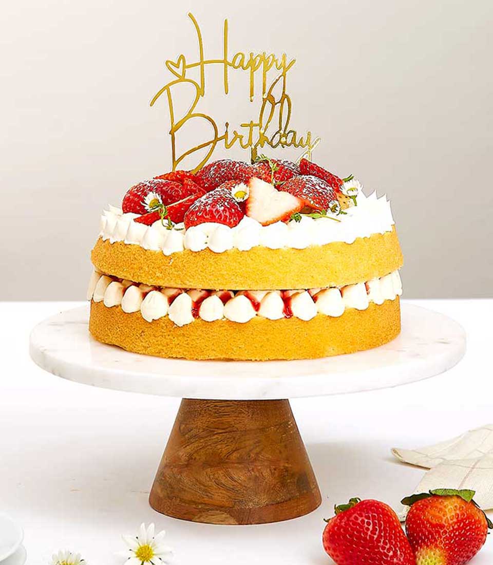 Strawberry cream birthday cake with fresh berries and white flowers on marble stand