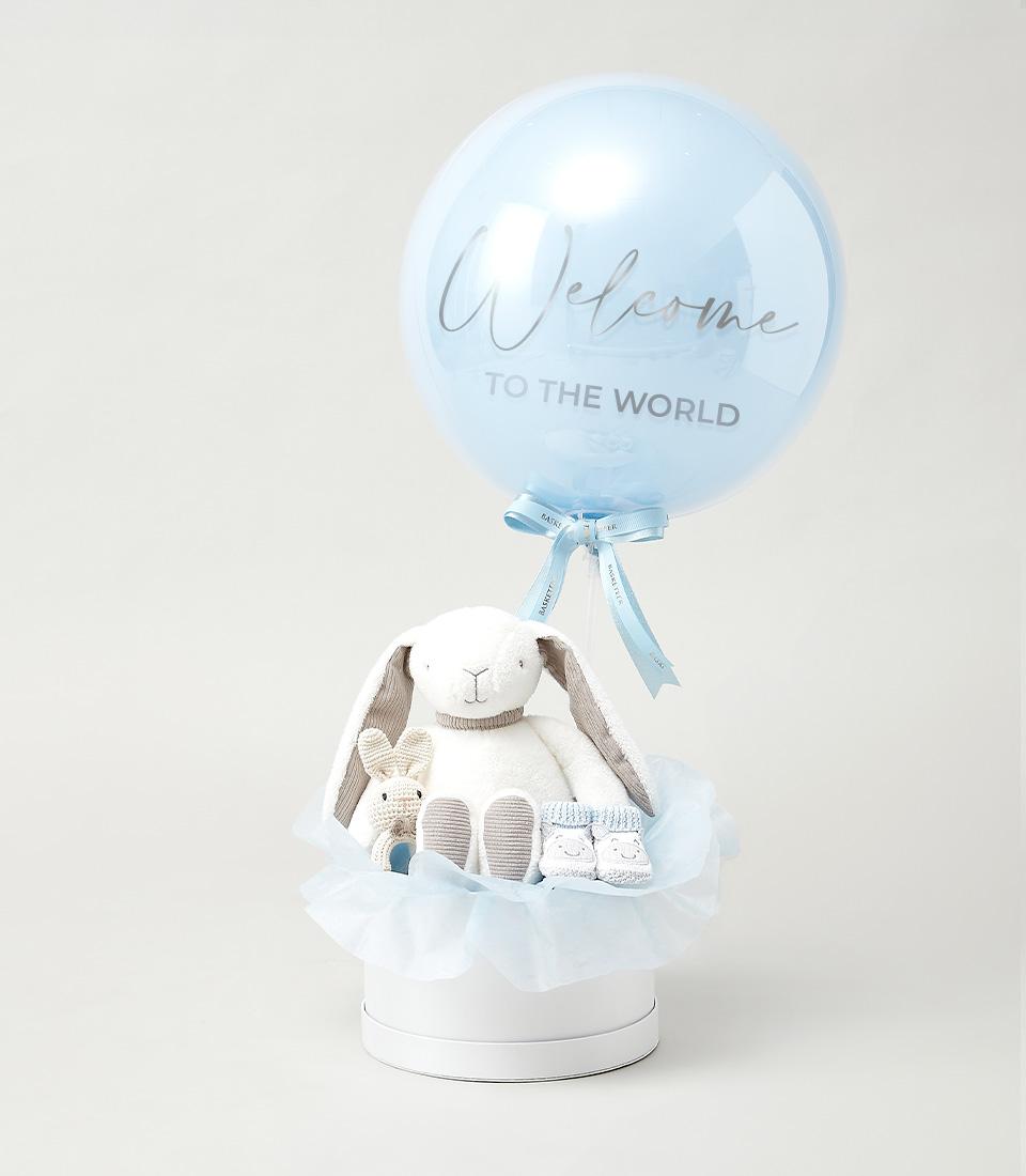 White round gift box with plush bunny, crocheted rattle, and blue baby booties for newborn welcome