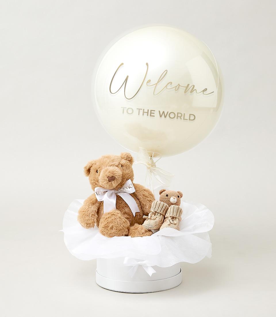 Elegant baby welcome hamper with gold script balloon, plush teddy bears, and crocheted booties in white gift box