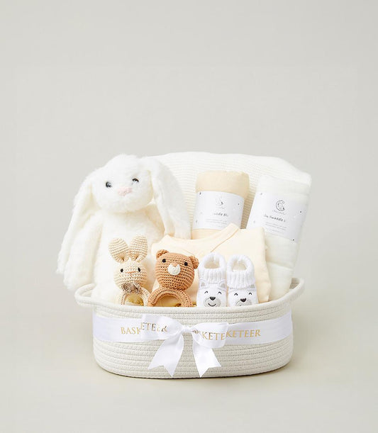 Warm white woven baby gift basket with plush bunny, crocheted rattles, and cream blankets for newborns