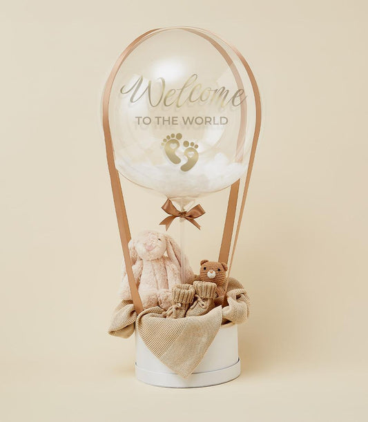 Luxury newborn gift hamper with hot air balloon design, plush bunny and teddy bear, knitted booties on cream backdrop