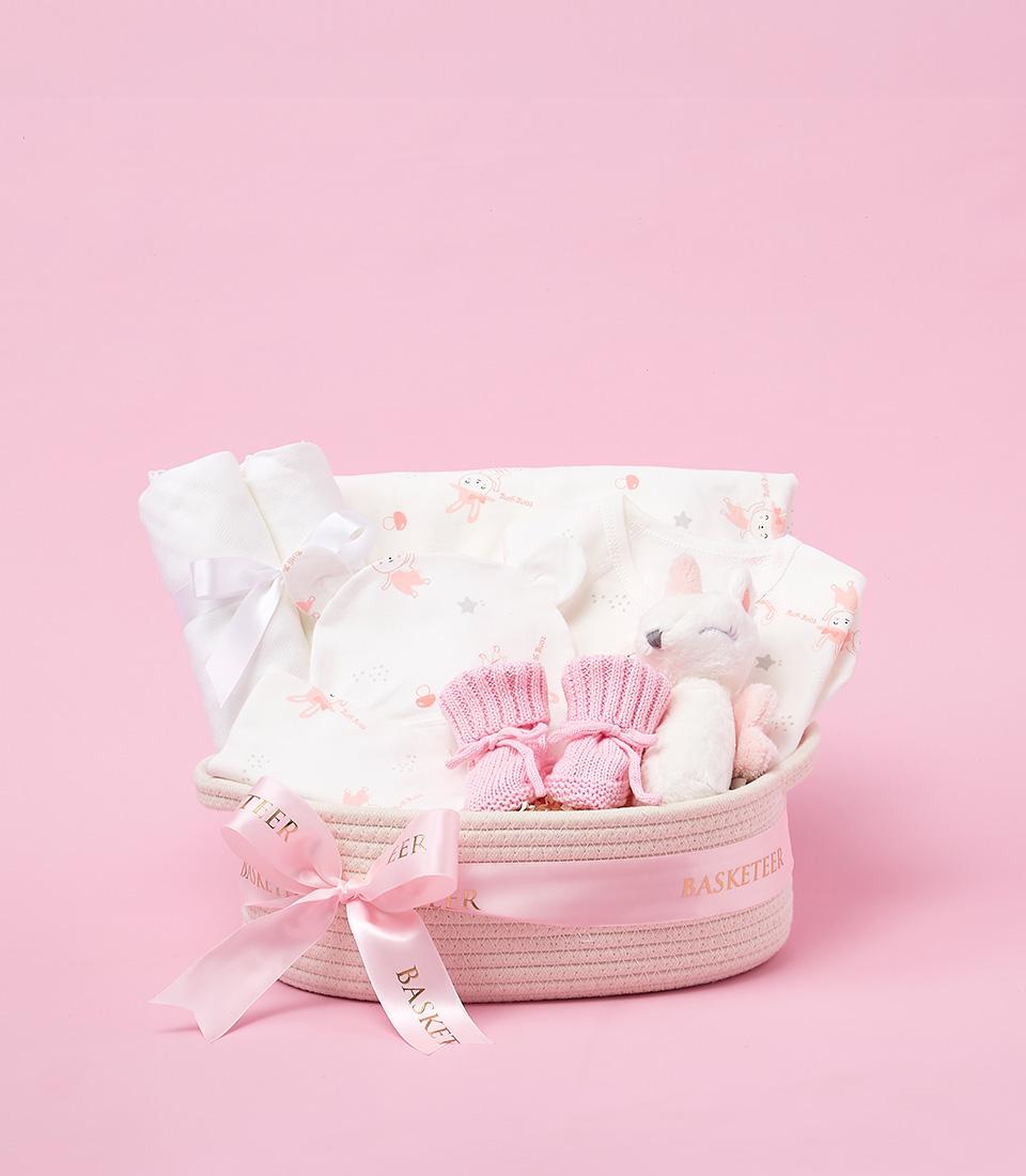 Soft pink woven baby gift basket with bunny-patterned clothing, booties, and plush toy for newborns