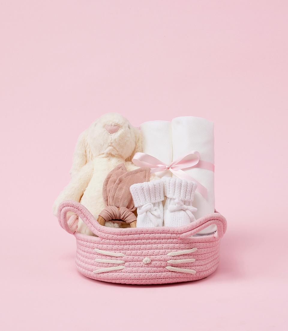 Pink baby gift basket with plush bunny, blankets, wooden teether, and booties for newborn girls