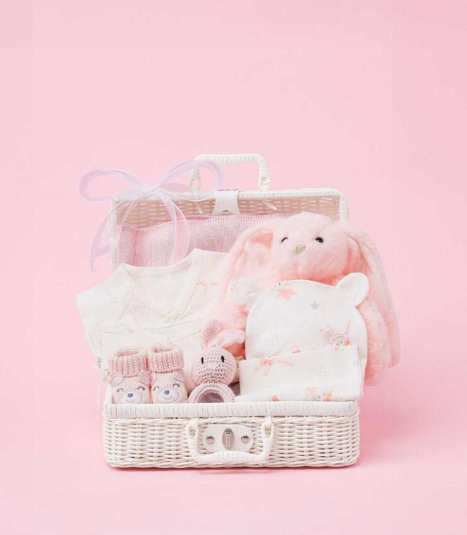 Luxury baby girl gift basket with plush bunny toy, bunny-print blanket, bodysuit, and booties in white wicker suitcase