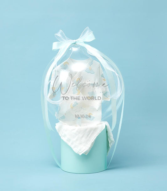 Light blue welcome baby boy gift set with cloud-patterned onesie, muslin cloth, and "Welcome to the World" packaging