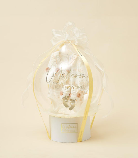 White baby outfit and booties in sheer balloon sphere with welcome gift box and yellow Basketeer ribbon