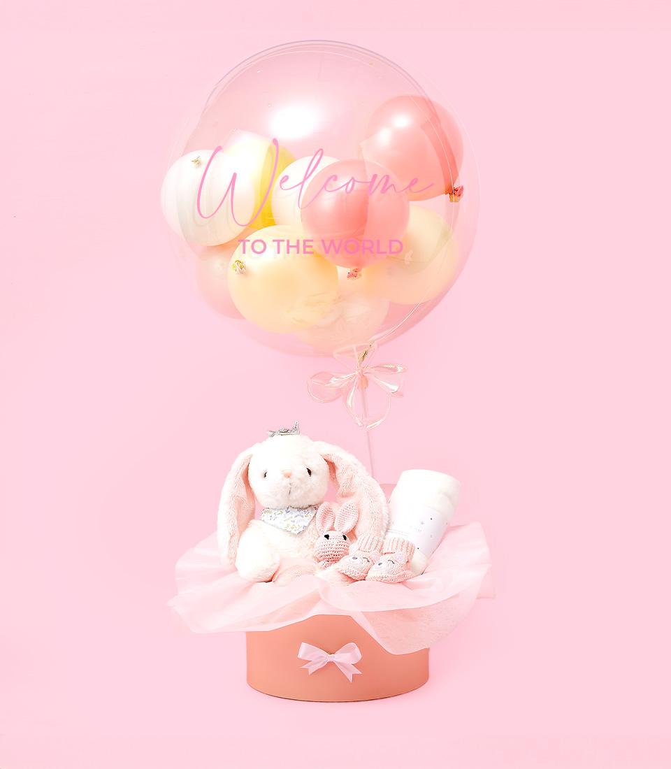 Sweet pastel baby gift set with welcome balloon, plush bunny, and crocheted booties in peach box