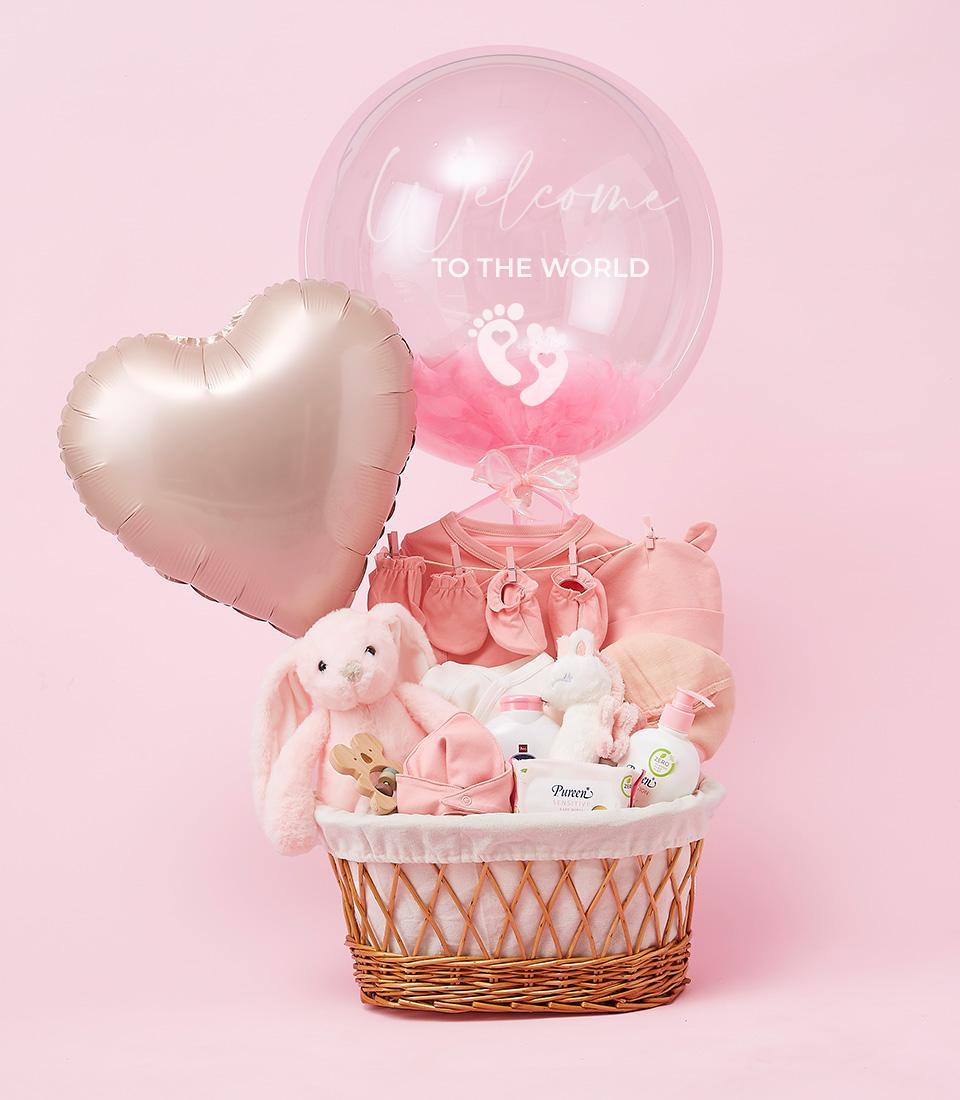 Charming Baby Girl Welcome Basket with pink clothes, plush bunnies, and baby care products in woven wicker
