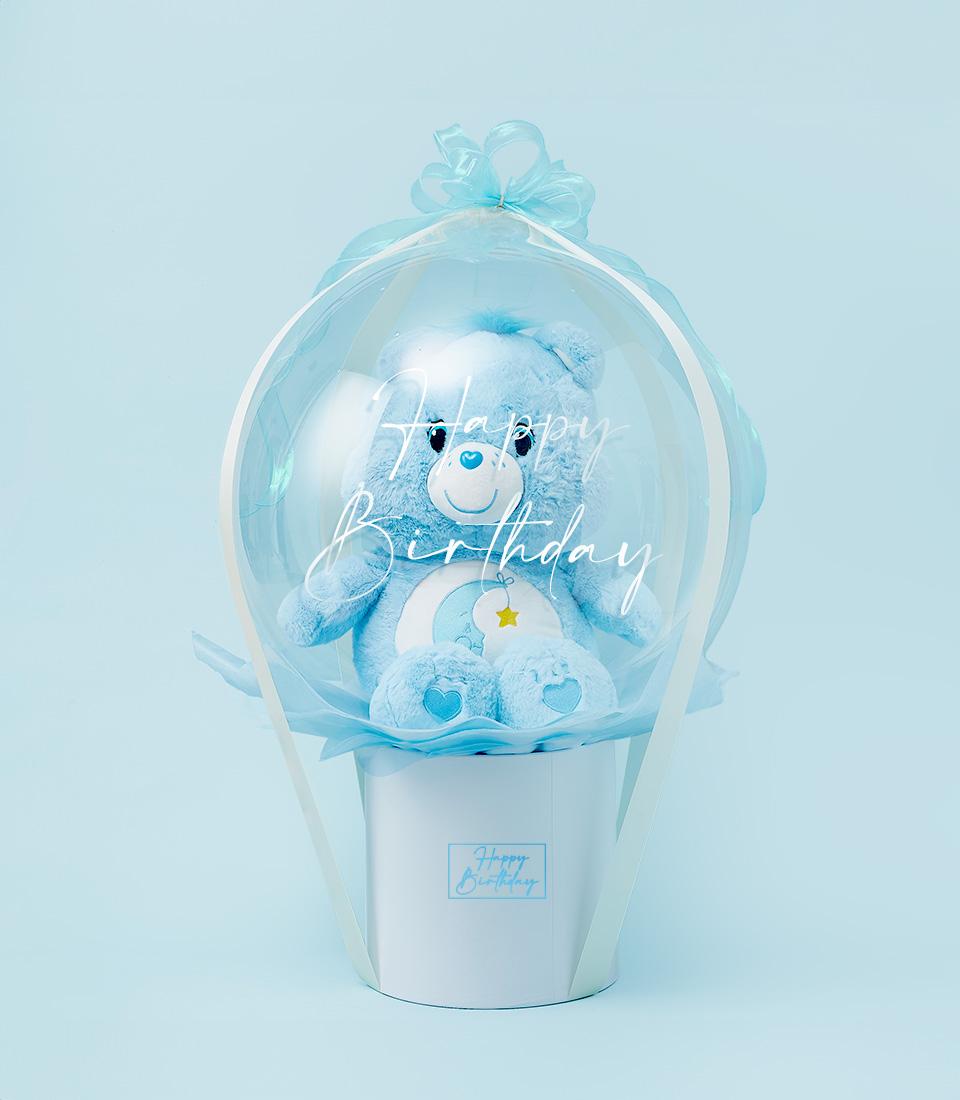 Light blue Bedtime Bear plush toy in clear birthday balloon with ribbon, presented in white cylindrical gift box