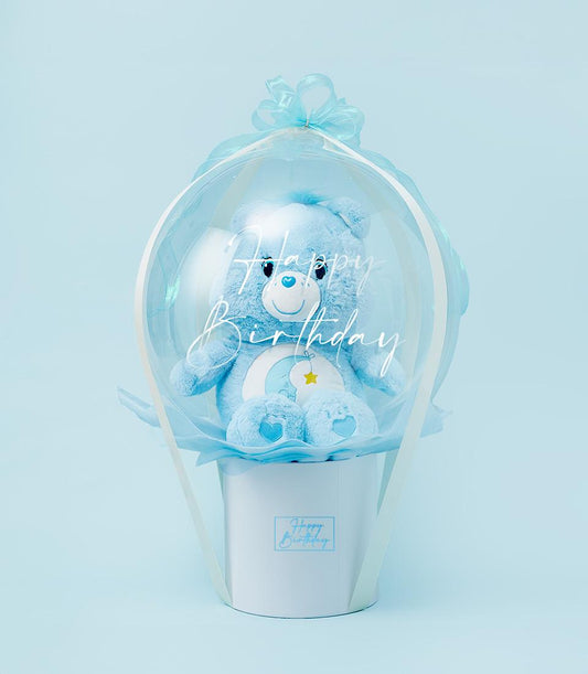 Light blue Bedtime Bear plush toy in clear birthday balloon with ribbon, presented in white cylindrical gift box