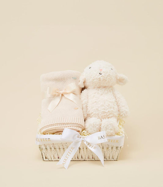 Cream knit baby blanket and plush lamb toy in white woven gift basket with pink ribbon