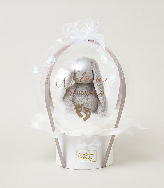 Grey plush bunny in clear welcome balloon, white gift box with gold accents, new baby hamper