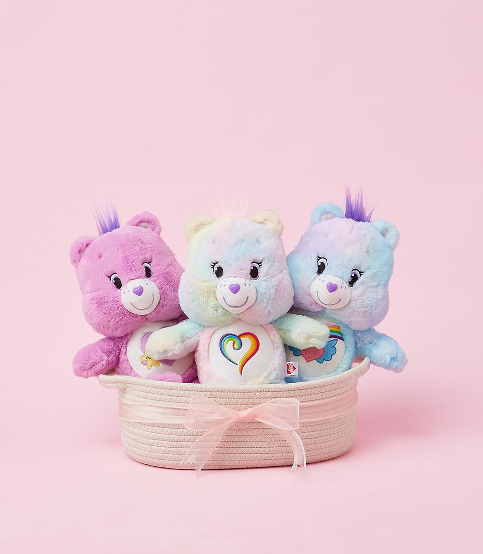Pastel plush Care Bears trio in woven pink basket with rainbow tie-dye and heart belly badges