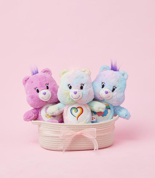 Pastel plush Care Bears trio in woven pink basket with rainbow tie-dye and heart belly badges