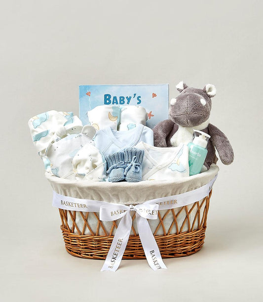 Light blue and white newborn gift basket with organic baby essentials, plush hippo toy, and clothing for new parents