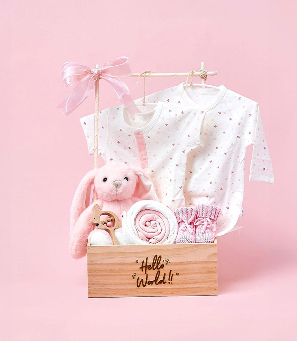 Pink baby gift hamper with plush bunny, wooden teether, blanket, and booties in light wooden crate
