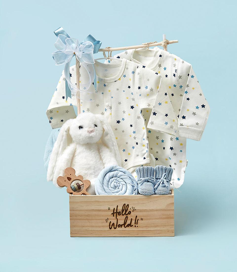Light wooden crate newborn gift set with plush bunny, blue blanket, bear rattle, booties, and star-patterned bodysuits on