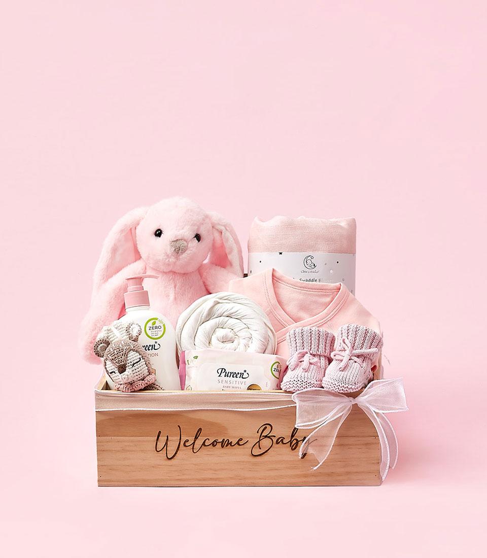 Wooden baby gift box with pink and white essentials, plush bunny, lotion, swaddle, and booties for newborn welcome gifting