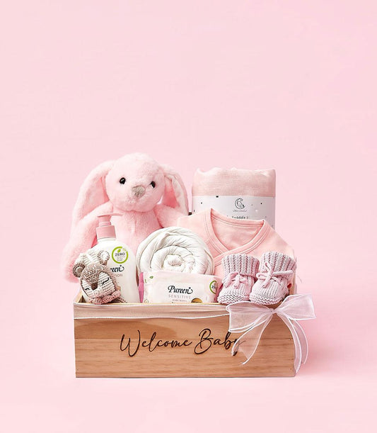 Wooden baby gift box with pink and white essentials, plush bunny, lotion, swaddle, and booties for newborn welcome gifting