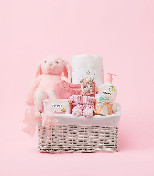 Pink baby gift basket with plush bunny, muslin blanket, bodysuit, booties, and care essentials