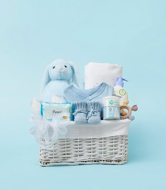 Light blue baby gift basket with plush bunny, bodysuit, booties, and newborn essentials in white wicker