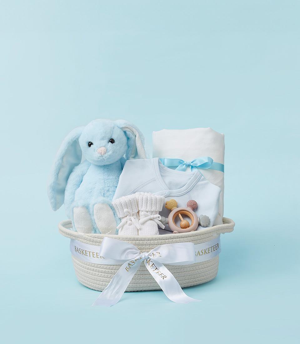 Woven baby gift basket with light blue plush bunny, onesie, knitted booties, teether, and soft blanket