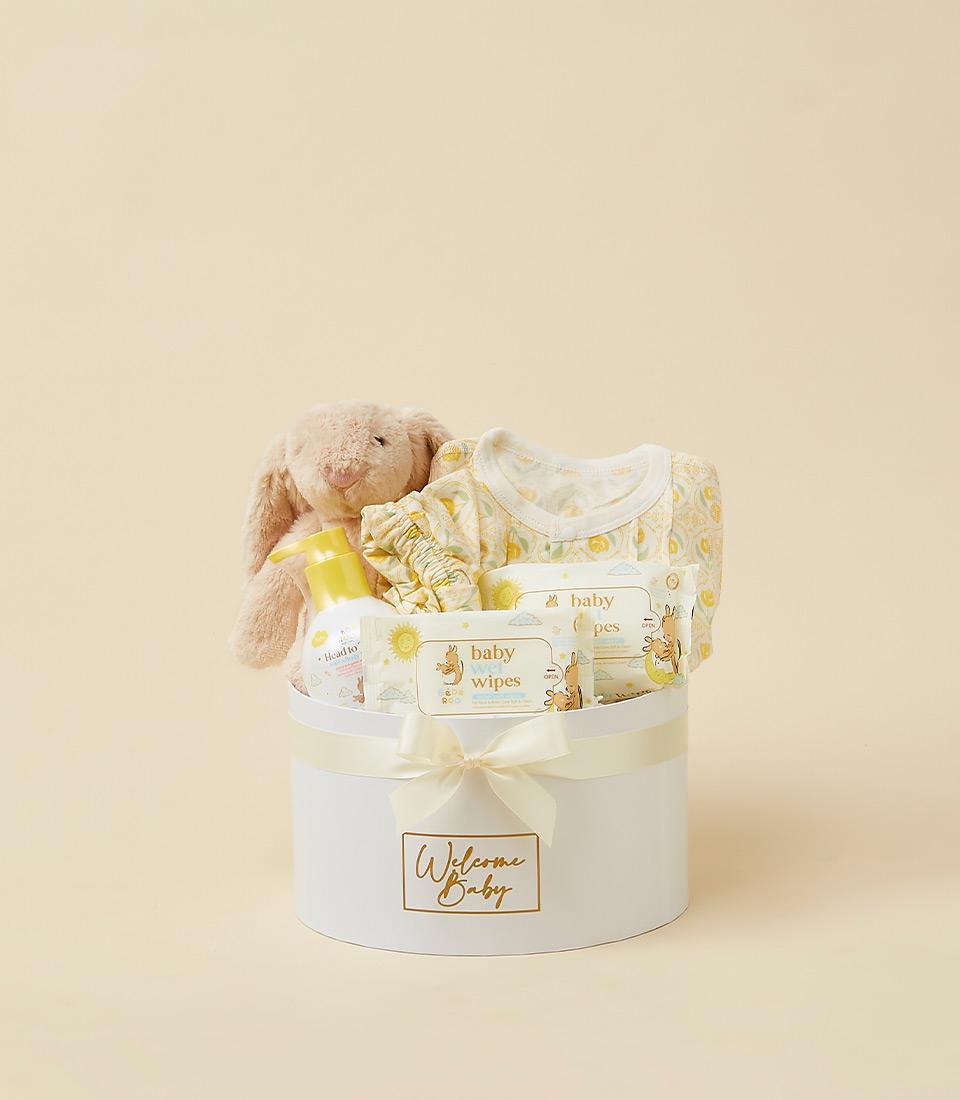 Newborn welcome gift set with plush bunny, yellow onesie, baby wash, and wipes in white cylindrical box with cream ribbon