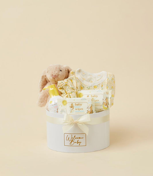 Newborn welcome gift set with plush bunny, yellow onesie, baby wash, and wipes in white cylindrical box with cream ribbon