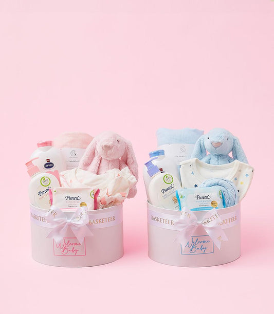 Gentle pink and blue baby welcome gift boxes with plush bunnies, soft blankets, and bath essentials