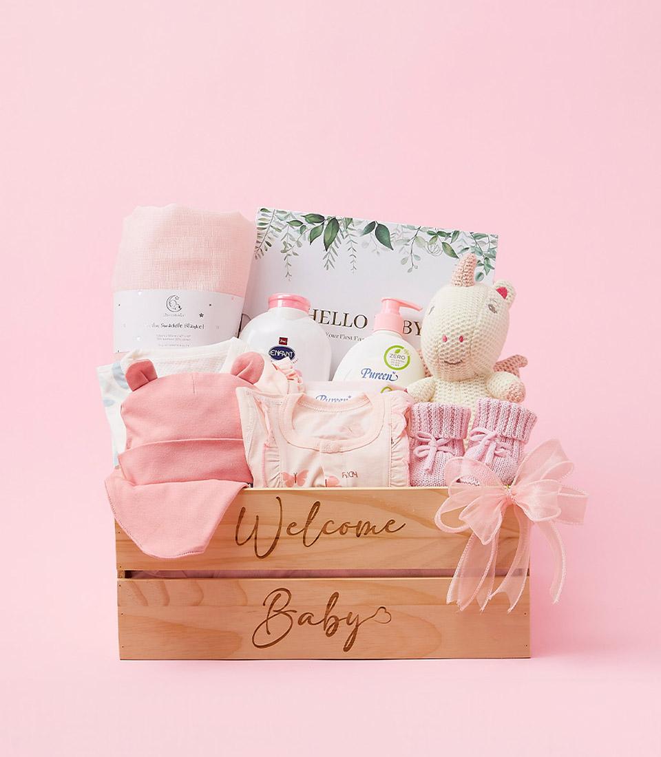 Light wooden crate welcome baby gift set with pink swaddle, hat, booties, butterfly outfit, and plush toy
