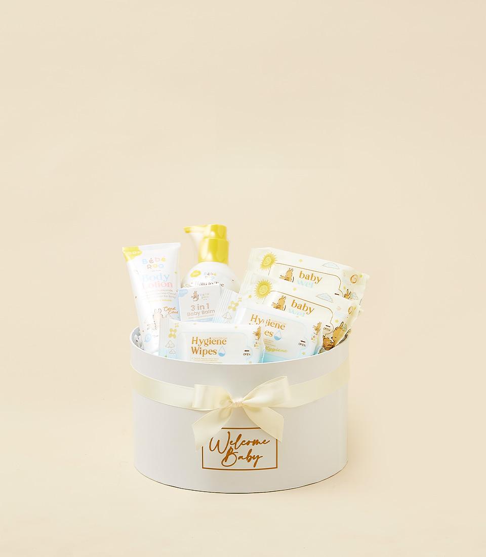 White cylindrical newborn gift box with cream ribbon, filled with baby lotion, balm, and wipes for gentle skincare