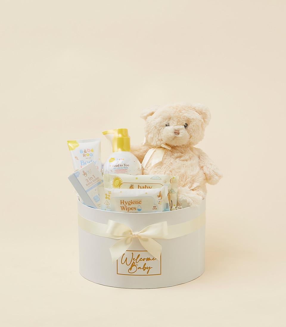 Curated newborn care gift set with teddy bear, baby cream, wash, and wipes in cream ribbon-tied box