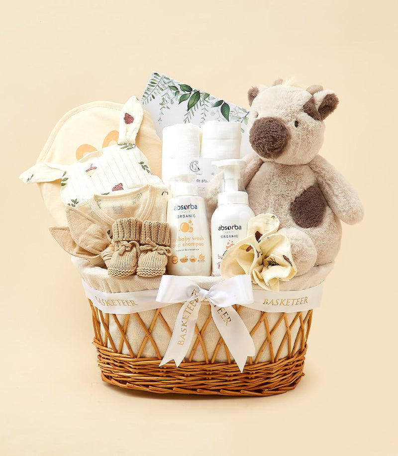Woven wicker baby gift basket with organic wash, spotted plush cow, bunny onesie, and booties