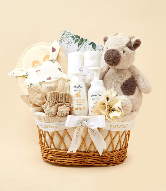 Woven wicker baby gift basket with organic wash, spotted plush cow, bunny onesie, and booties