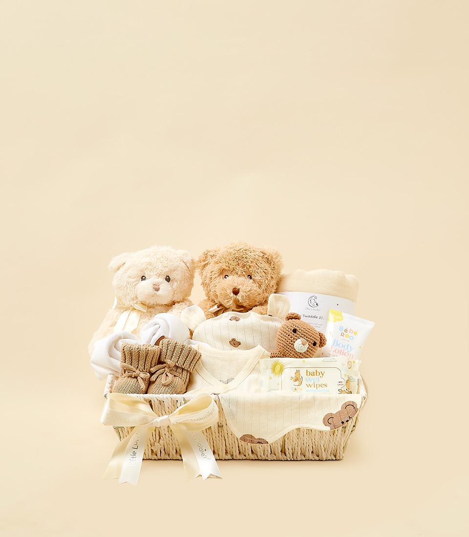 Woven cream gift basket with plush teddy bears, baby clothing, booties, and bath essentials for newborns