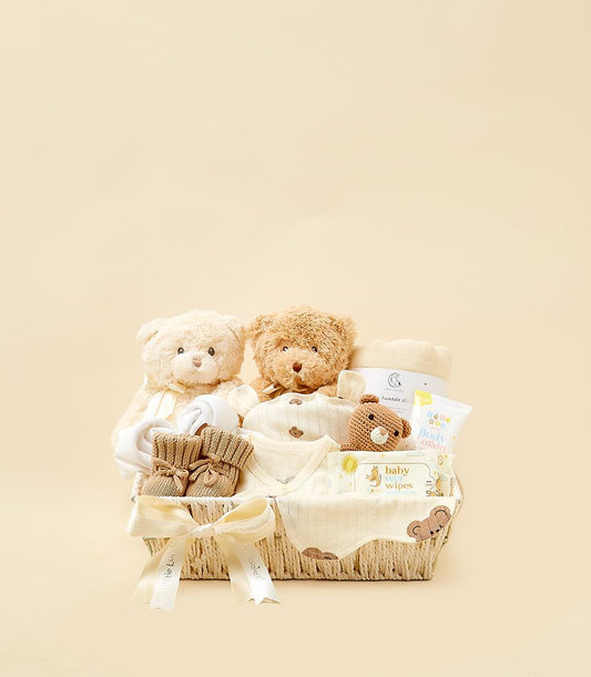 Woven cream gift basket with plush teddy bears, baby clothing, booties, and bath essentials for newborns