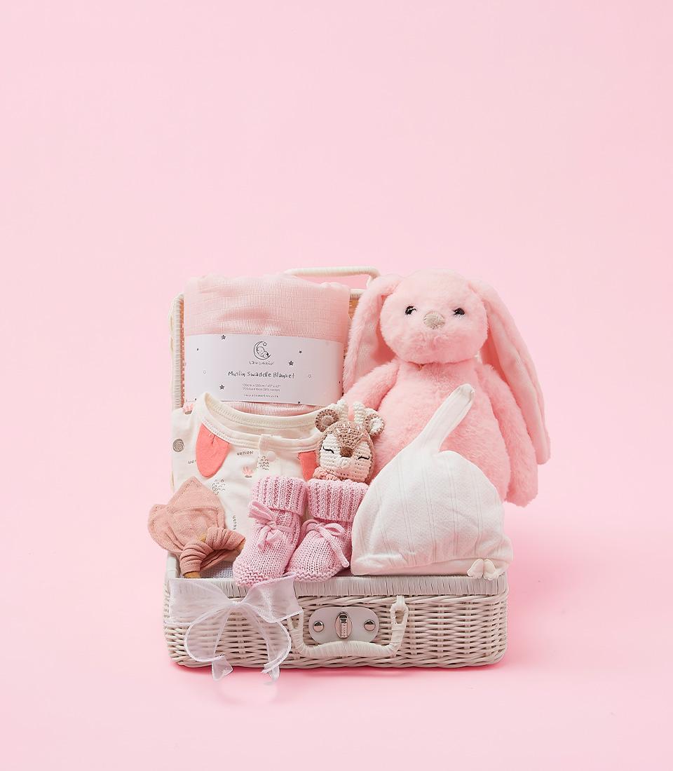Charming baby gift set in white wicker suitcase with pink muslin blanket, plush bunny toy, booties, and knitted hat