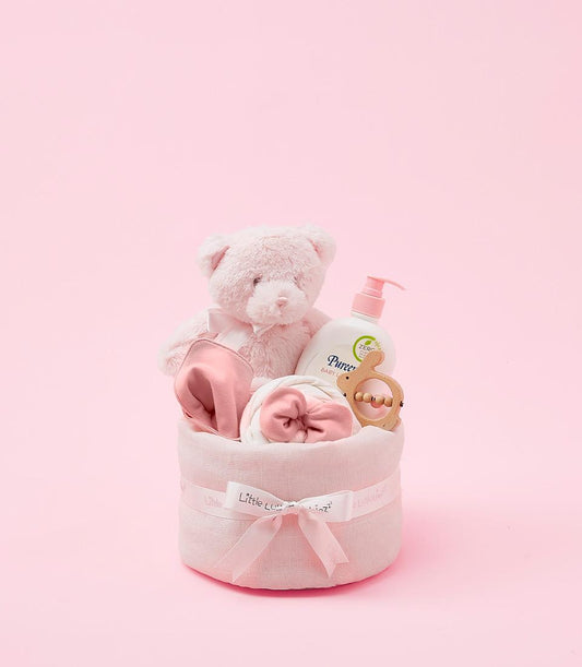 Pink newborn baby girl gift set with plush teddy, blanket, lotion, and wooden teether in luxury hamper