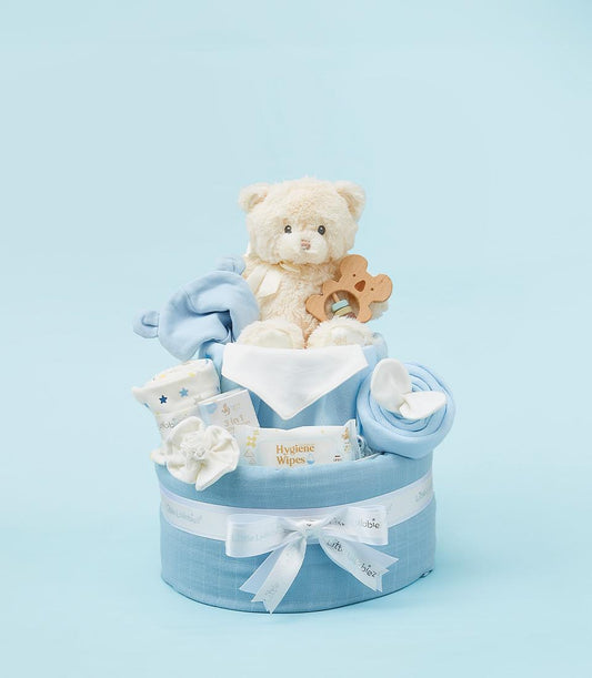 Blue and white two-tiered baby gift hamper with plush teddy bear, wipes, and soft essentials for newborns