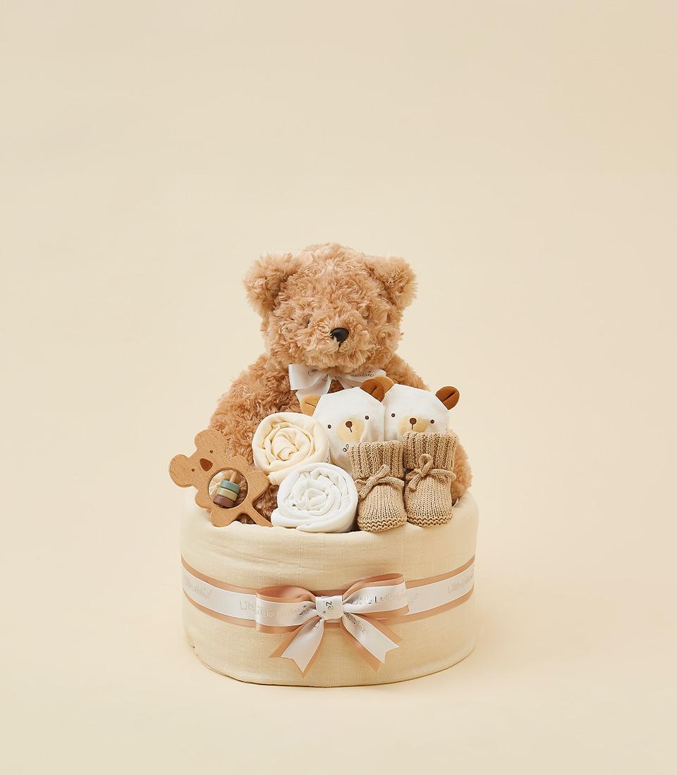 Neutral newborn gift basket with teddy bear, plush rattles, wooden rattle, and beige booties in fabric-wrapped container