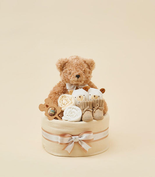 Neutral newborn gift basket with teddy bear, plush rattles, wooden rattle, and beige booties in fabric-wrapped container