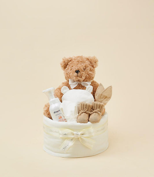 Soft cream diaper cake with teddy bear, baby booties, and organic care products for newborns
