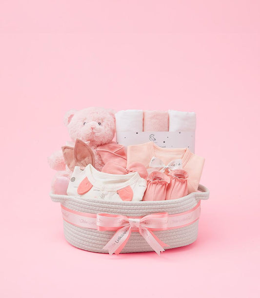 Pink baby gift basket with teddy bear, clothing, and star-printed blankets for newborns