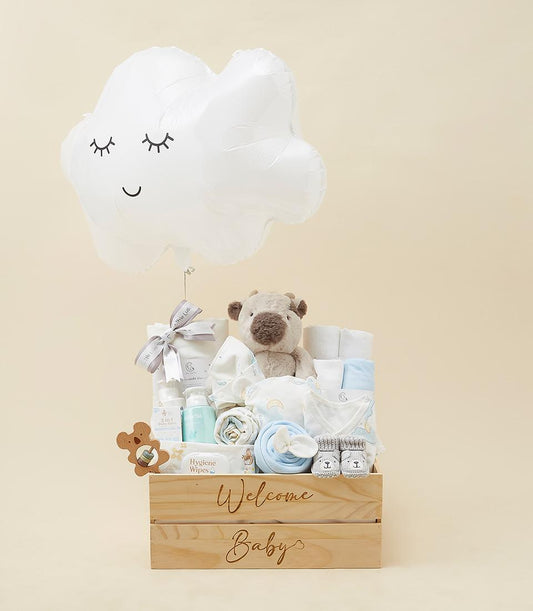 Welcome Baby gift hamper with plush toy, booties, clothing, care essentials, and cloud balloon in wooden crate
