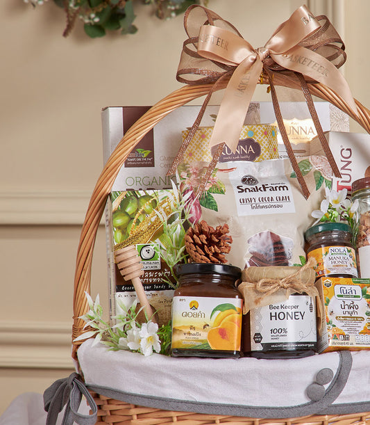 Woven wicker gift basket filled with coconut, honey, and gourmet snacks, tied with gold ribbon