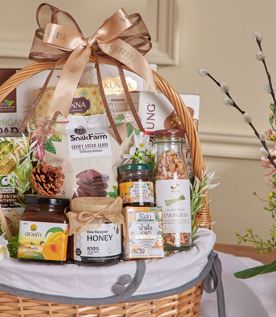 Light woven wicker gift basket with honey jars, manuka honey, fruit spread, coconut crisps, and lemongrass infusion, tied
