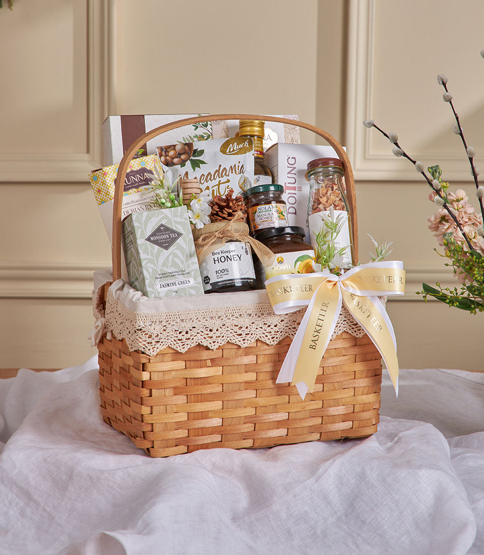 Premium wicker gift basket with jasmine tea, manuka honey, macadamia nuts, and wellness treats tied with yellow ribbon