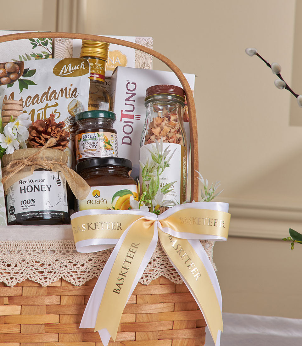 Woven gift basket with organic Thai honey, macadamia nuts, coconut products and dried botanicals, tied with gold ribbon